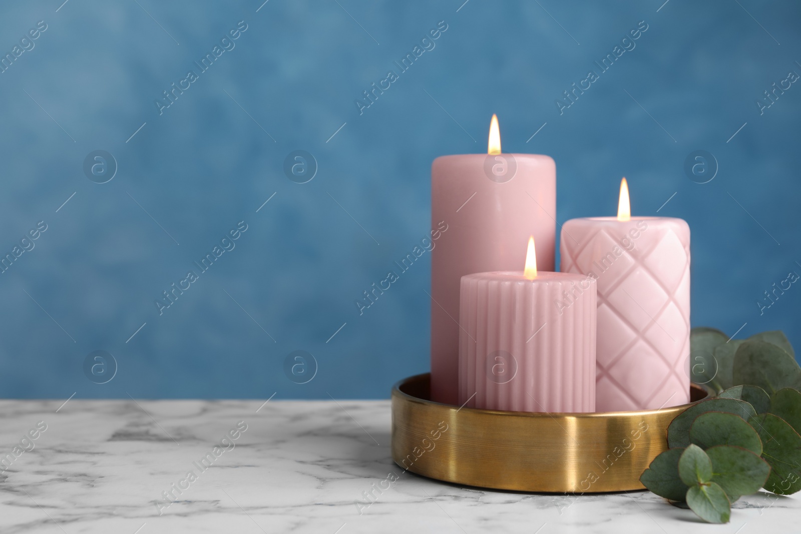 Photo of Beautiful candles and eucalyptus branch on white marble table against blue wall, space for text