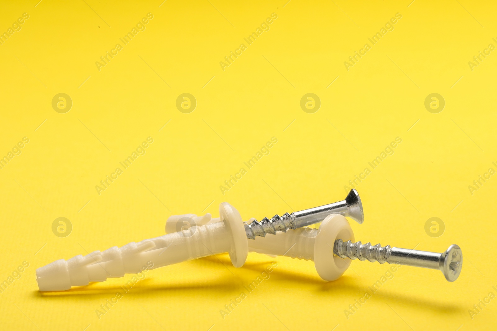 Photo of Metal screws and white straddling dowels, closeup. Space for text