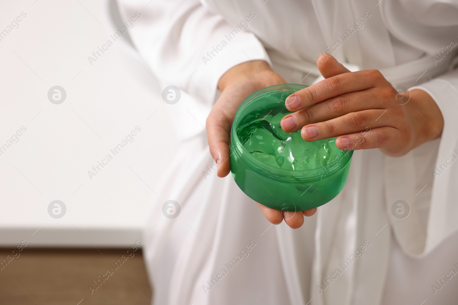 Photo of Young woman holding jar of aloe gel indoors, closeup. Space for text