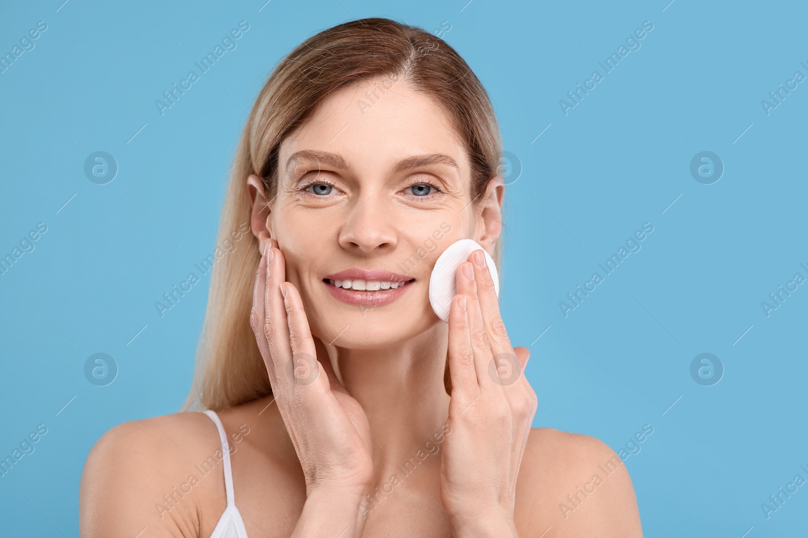 Photo of Beautiful woman removing makeup with cotton pad on light blue background