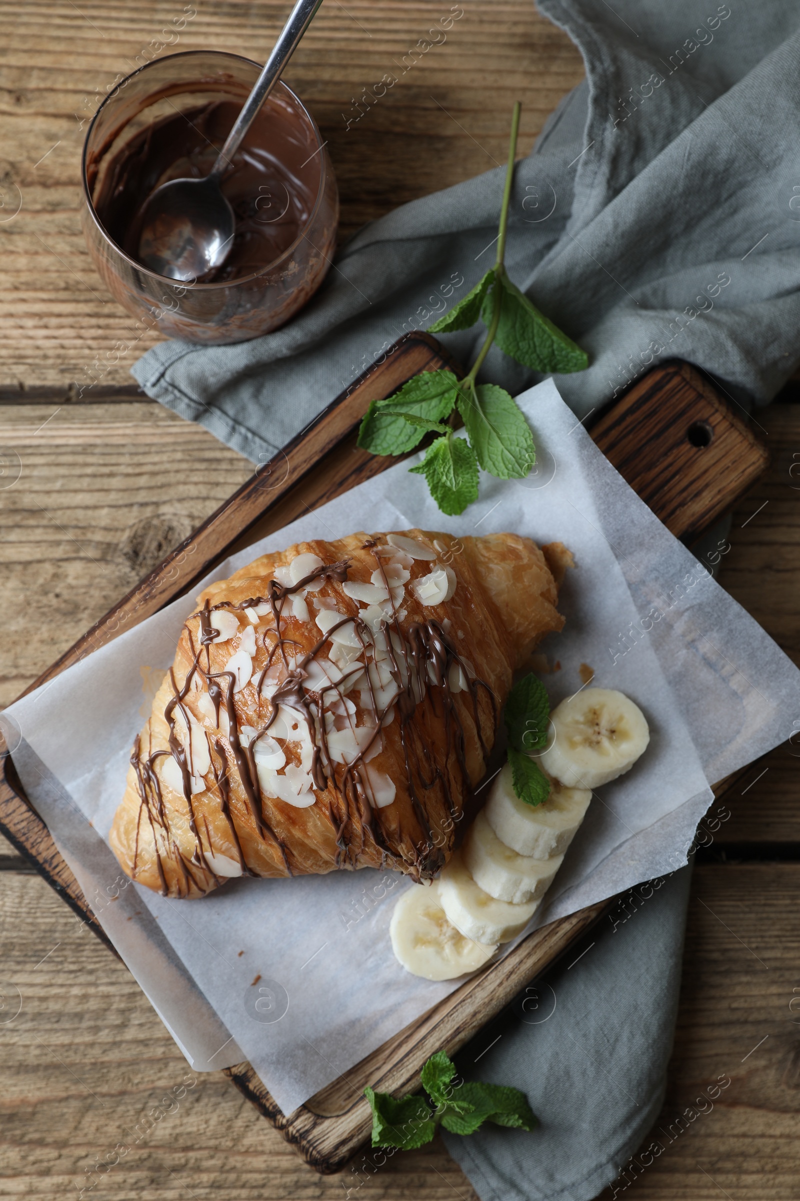 Photo of Delicious croissant with chocolate and banana on wooden table, flat lay