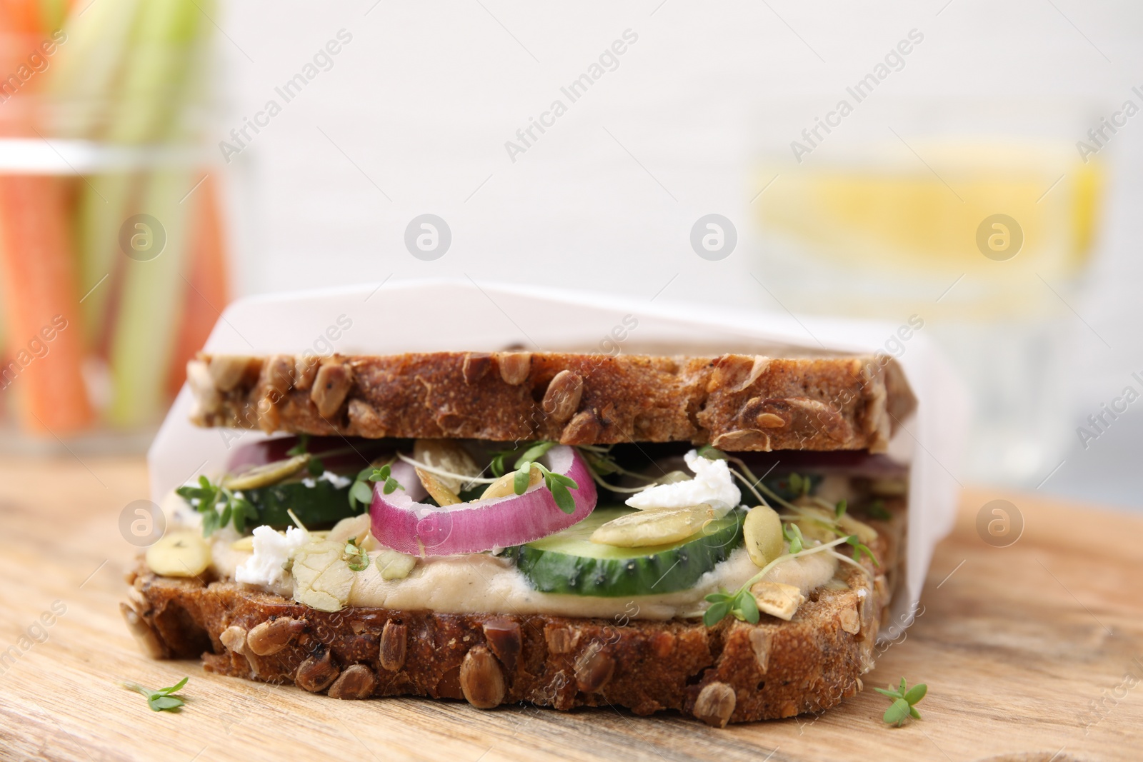 Photo of Tasty vegan sandwich with cucumber, onion, hummus and pumpkin seeds on wooden board, closeup