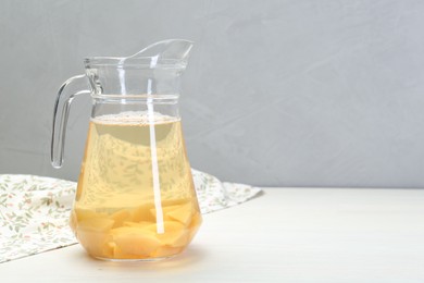 Delicious quince drink in glass jug on white wooden table, space for text