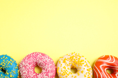 Photo of Delicious glazed donuts on yellow background, flat lay. Space for text