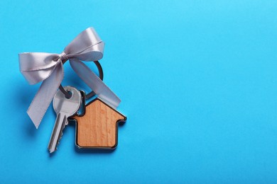 Photo of Key with trinket in shape of house and bow on light blue background, top view. Space for text. Housewarming party