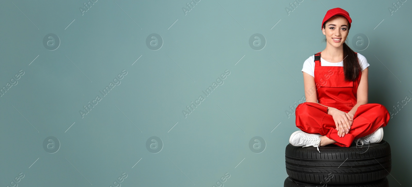 Image of Seller in uniform sitting on car tires against color background, space for text. Banner design