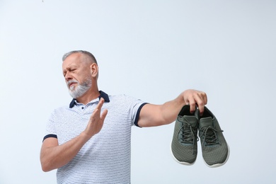 Man feeling bad smell from shoes on white background. Air freshener