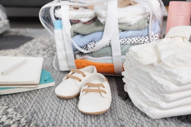 Photo of Packed bag with baby stuff, shoes and notebooks on carpet