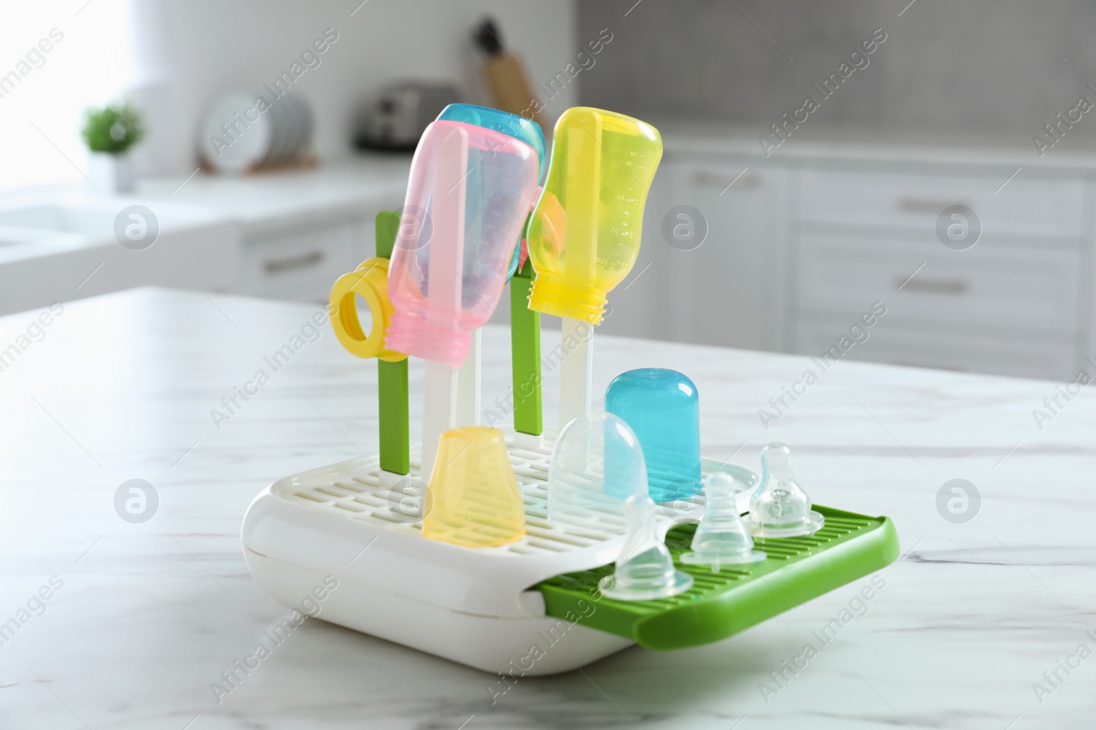 Photo of Dryer with baby bottles and nipples after sterilization on white marble table in kitchen