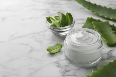 Jar with cream and cut aloe leaves on white marble table, closeup. Space for text