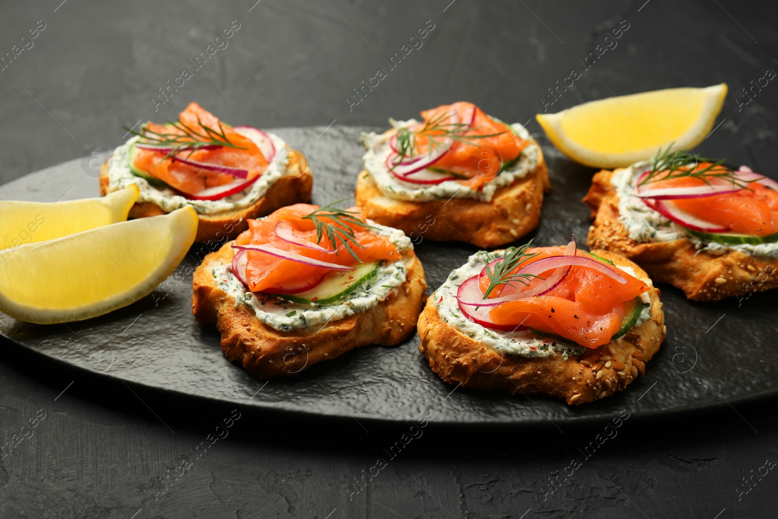 Photo of Tasty canapes with salmon, cucumber, radish and cream cheese on black table