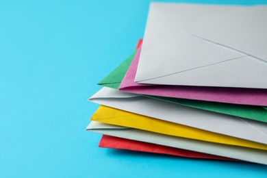 Photo of Stack of colorful paper envelopes on light blue background, closeup. Space for text
