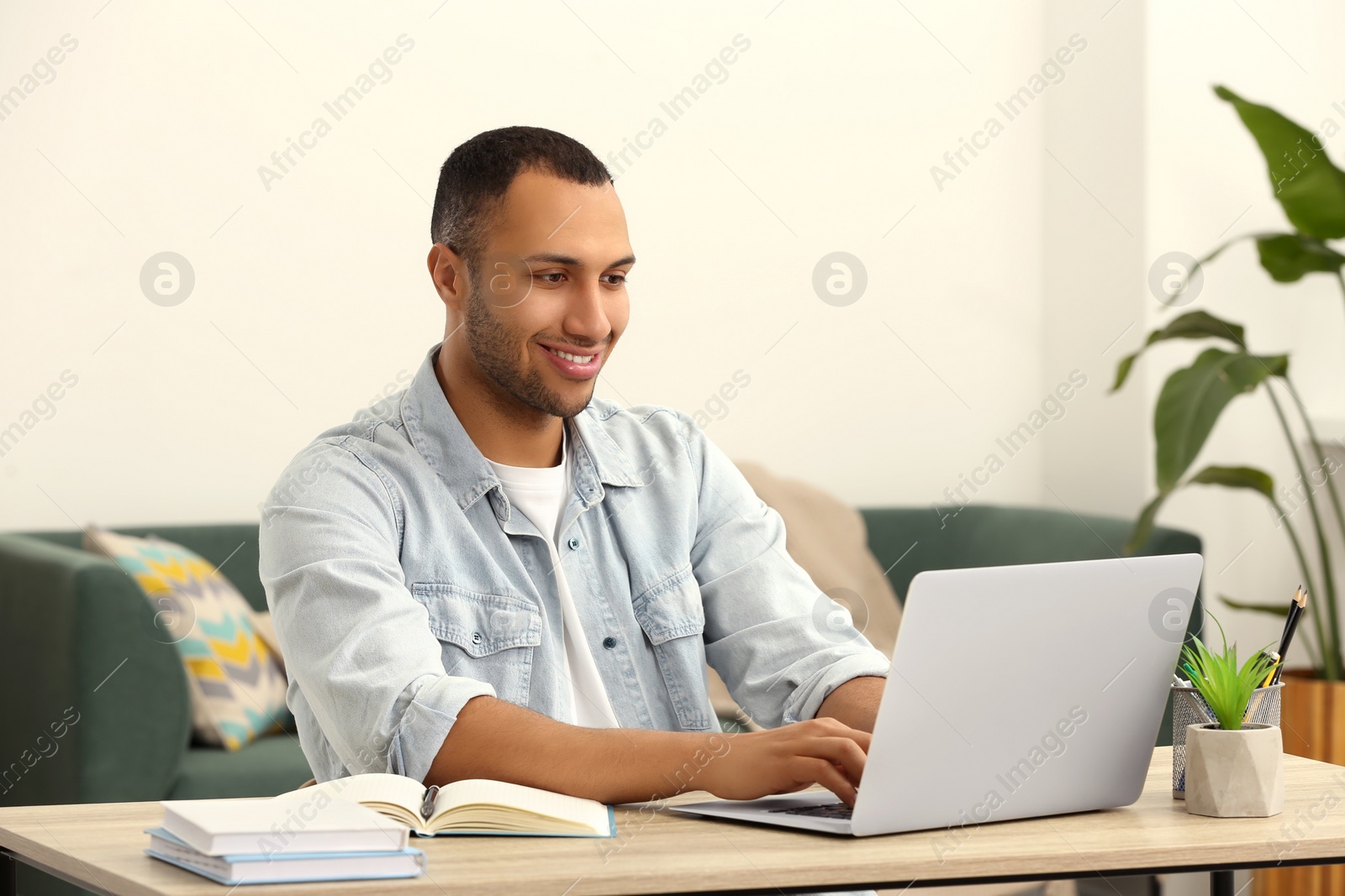 Photo of African American man typing on laptop at wooden table in room