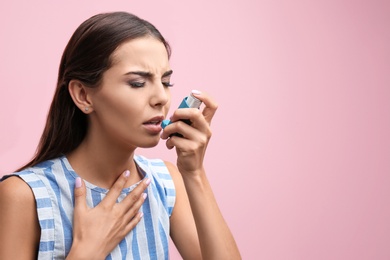 Young woman using asthma inhaler on color background. Space for text