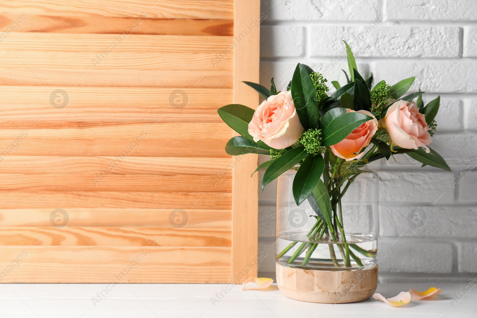 Photo of Bouquet with beautiful flowers in glass vase on white wooden table. Space for text