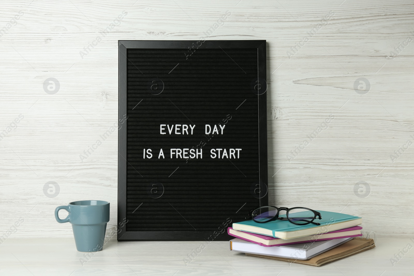 Photo of Black letter board with motivational quote Every Day is a Fresh Start, notebooks, glasses and cup on white wooden table