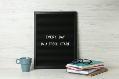 Photo of Black letter board with motivational quote Every Day is a Fresh Start, notebooks, glasses and cup on white wooden table