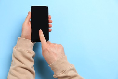 Photo of Man using smartphone on light blue background, top view. Space for text