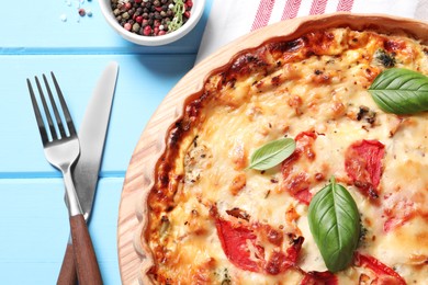 Photo of Tasty quiche with tomatoes, basil and cheese served on light blue wooden table, flat lay