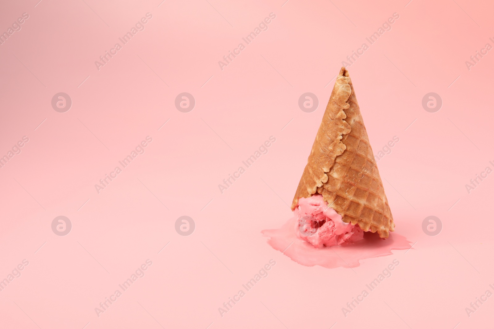 Photo of Melted ice cream in wafer cone on pink background. Space for text