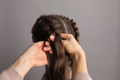 Professional stylist braiding woman's hair on grey background, closeup