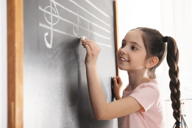 Photo of Little girl writing music notes on blackboard in classroom