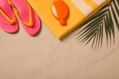 Photo of Beach towel, flip flops, sunscreen and palm leaf on sand, flat lay. Space for text