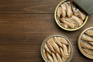 Open tin cans of sprats on wooden table, flat lay. Space for text