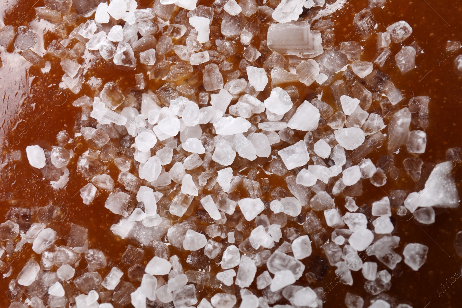 Photo of Delicious caramel sauce with sea salt as background, top view