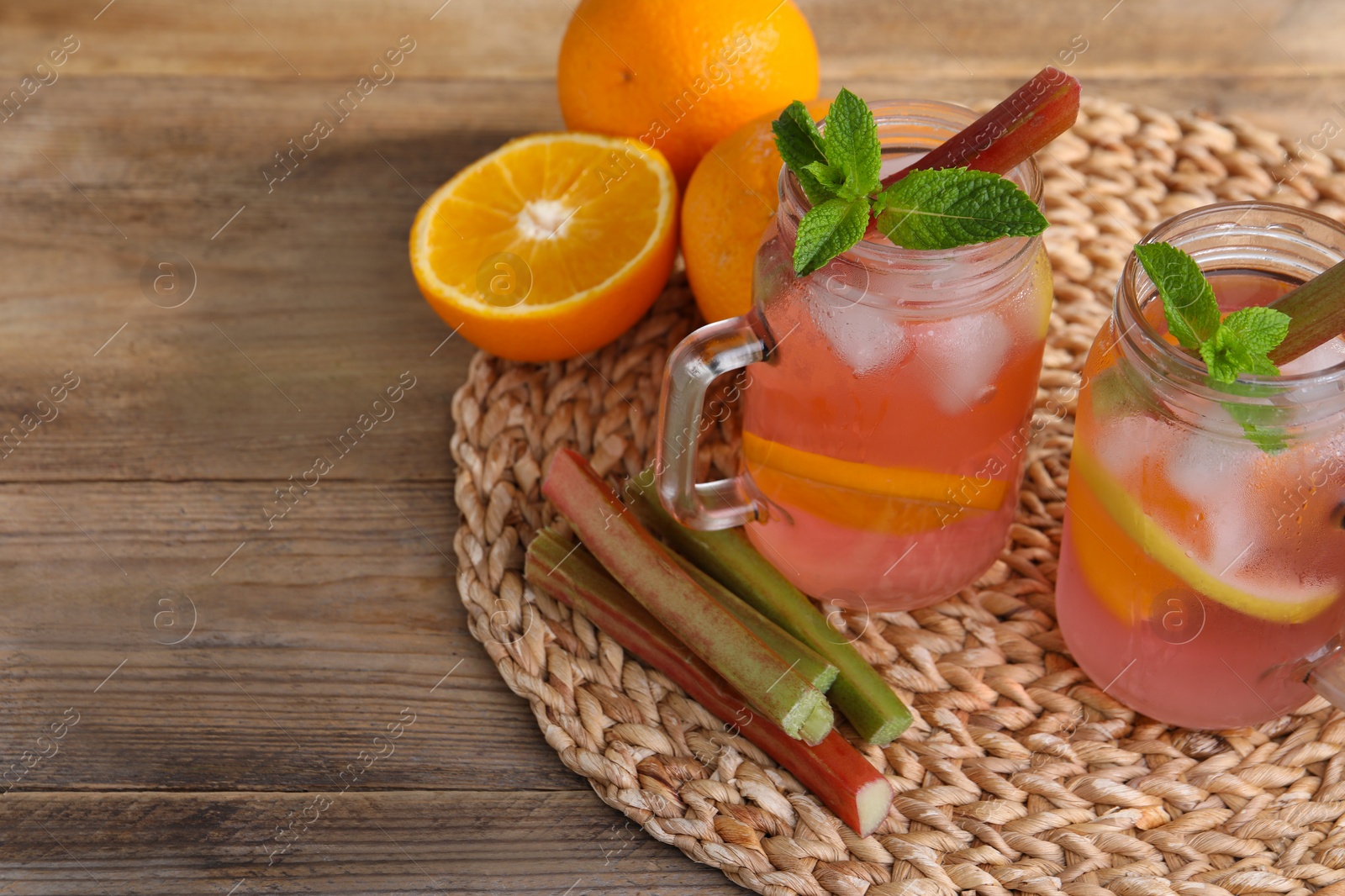 Photo of Mason jars of tasty rhubarb cocktail with citrus fruits on wooden table, space for text