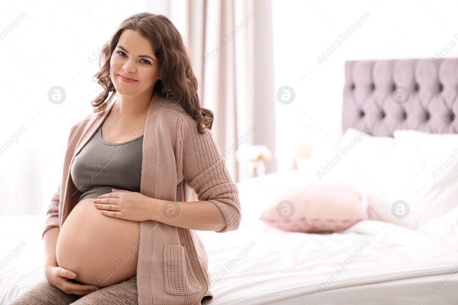 Photo of Young pregnant woman sitting on bed at home