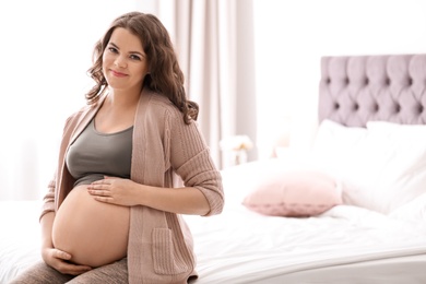 Young pregnant woman sitting on bed at home