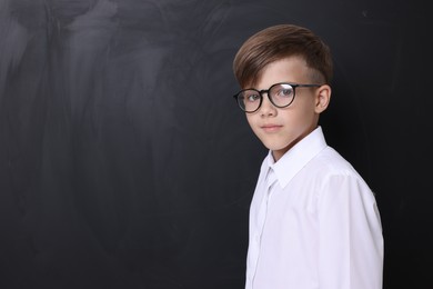 Cute schoolboy in glasses near chalkboard, space for text