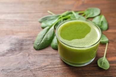 Photo of Glass with delicious detox juice and spinach on wooden background