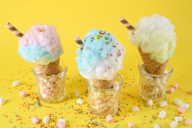 Photo of Sweet cotton candies in waffle cones and marshmallows on yellow background, closeup