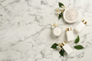 Photo of Beautiful jasmine flowers, skin care products and sea salt on white marble table, flat lay. Space for text