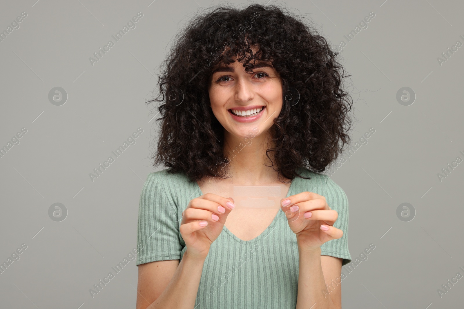 Photo of Young woman holding teeth whitening strips on grey background