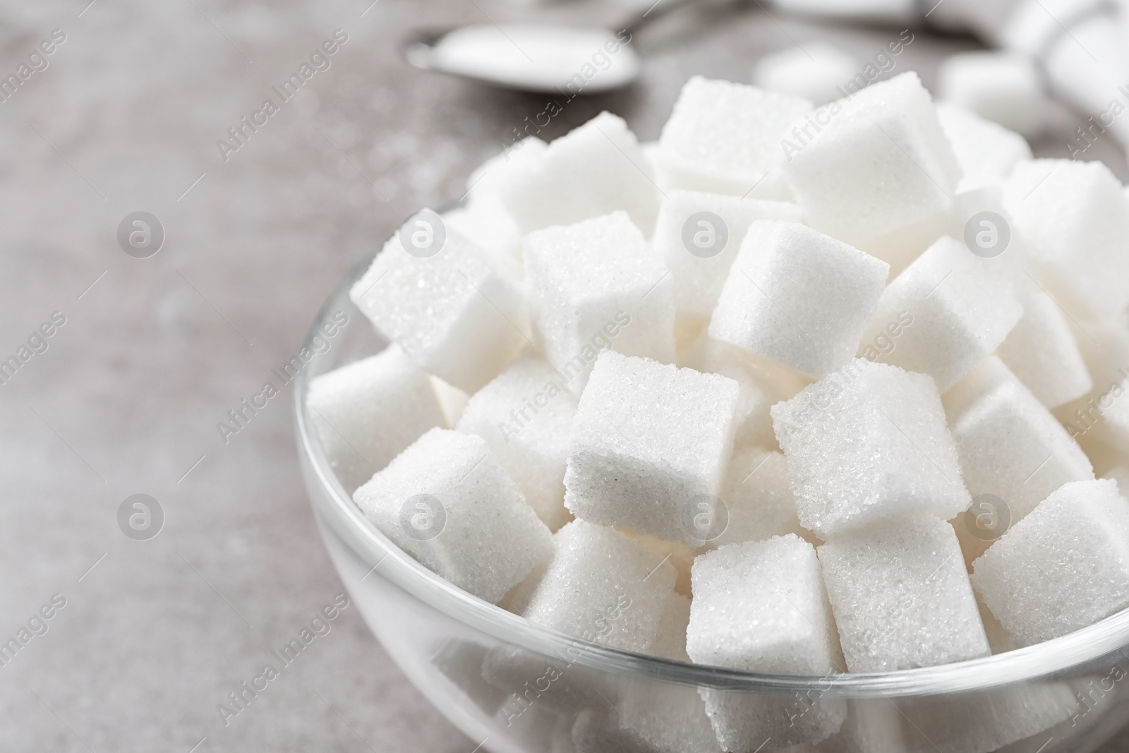 Photo of Refined sugar cubes in glass bowl on grey table, closeup