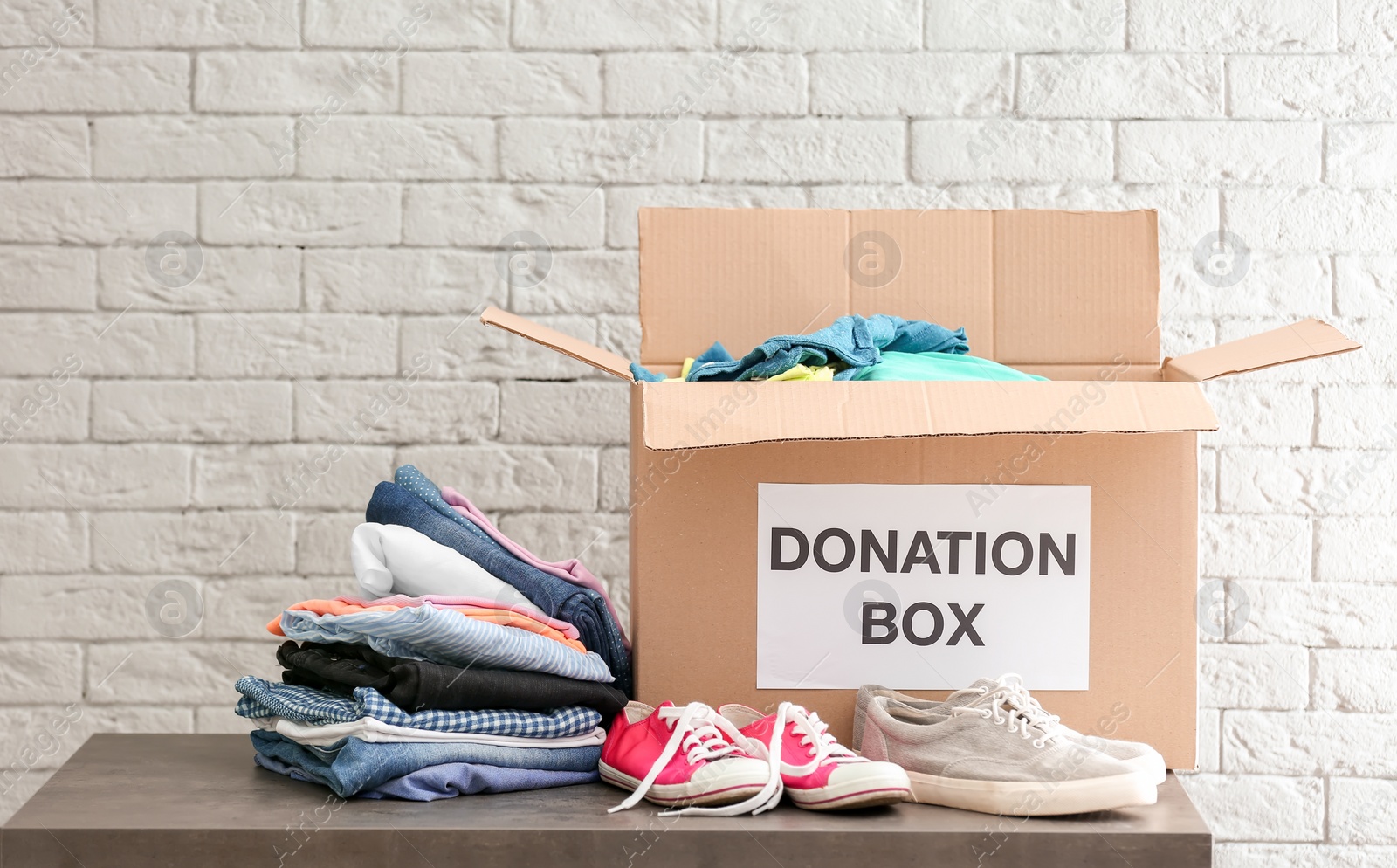 Photo of Donation box with clothes and shoes on table against brick wall