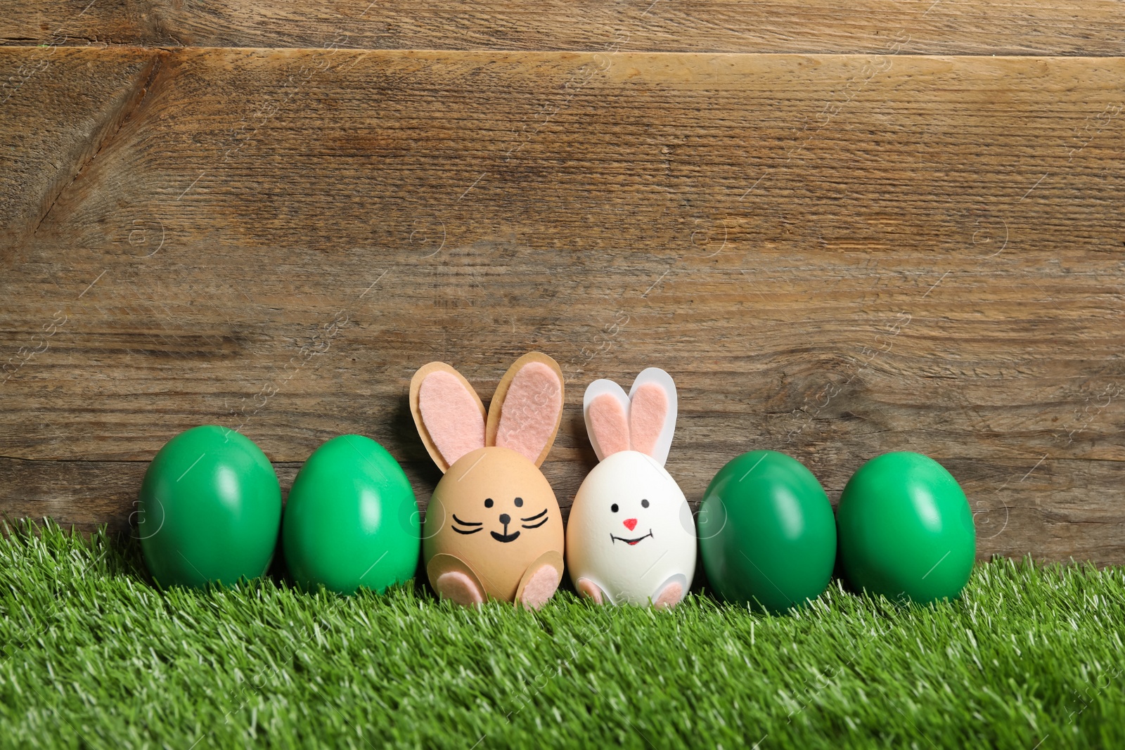 Photo of Two eggs as Easter bunnies among others on green grass against wooden background