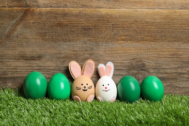 Two eggs as Easter bunnies among others on green grass against wooden background