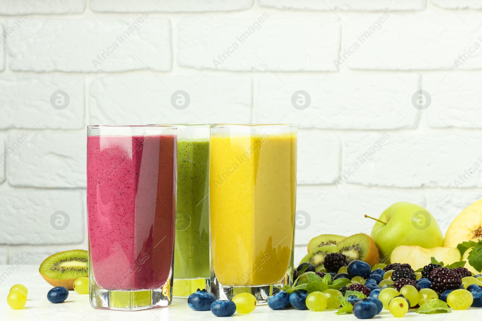 Photo of Fresh colorful fruit smoothies and ingredients on table against white brick wall. Space for text