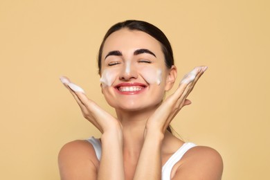 Photo of Happy woman with cleansing foam on face against beige background