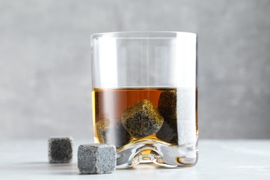 Whiskey stones and drink in glass on light table, closeup