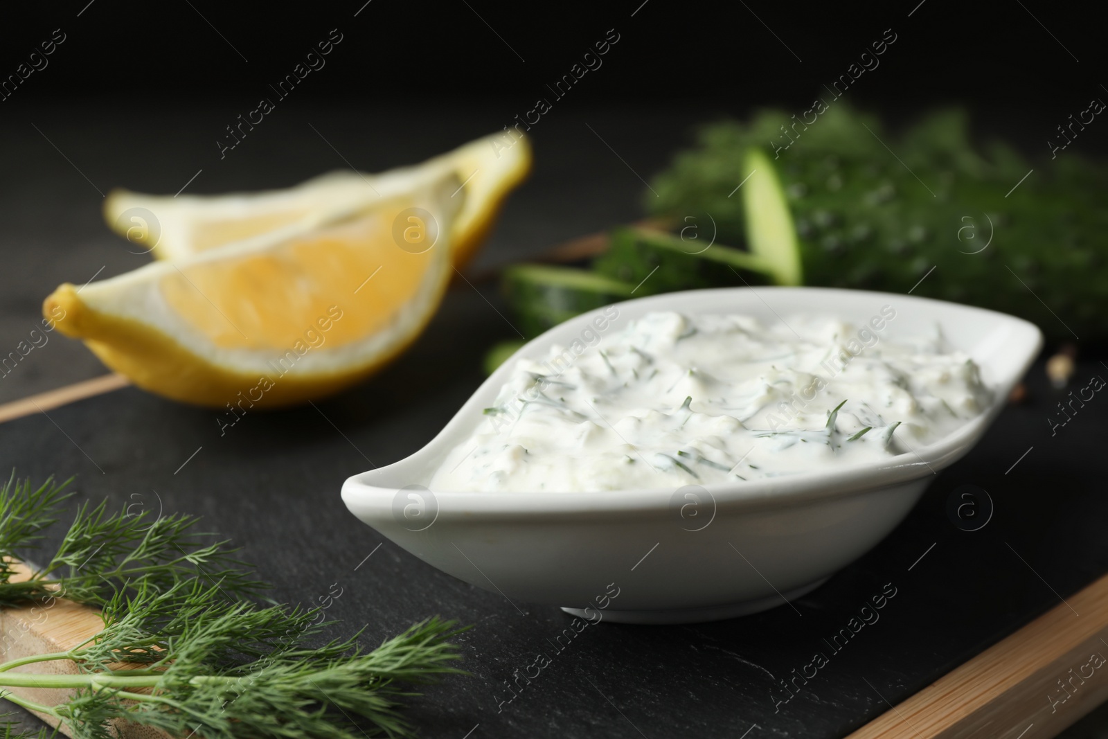 Photo of Dish of Tzatziki sauce with lemon slices, cucumber and dill on black board