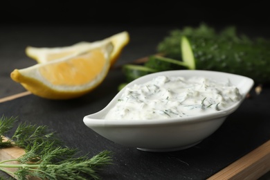 Photo of Dish of Tzatziki sauce with lemon slices, cucumber and dill on black board