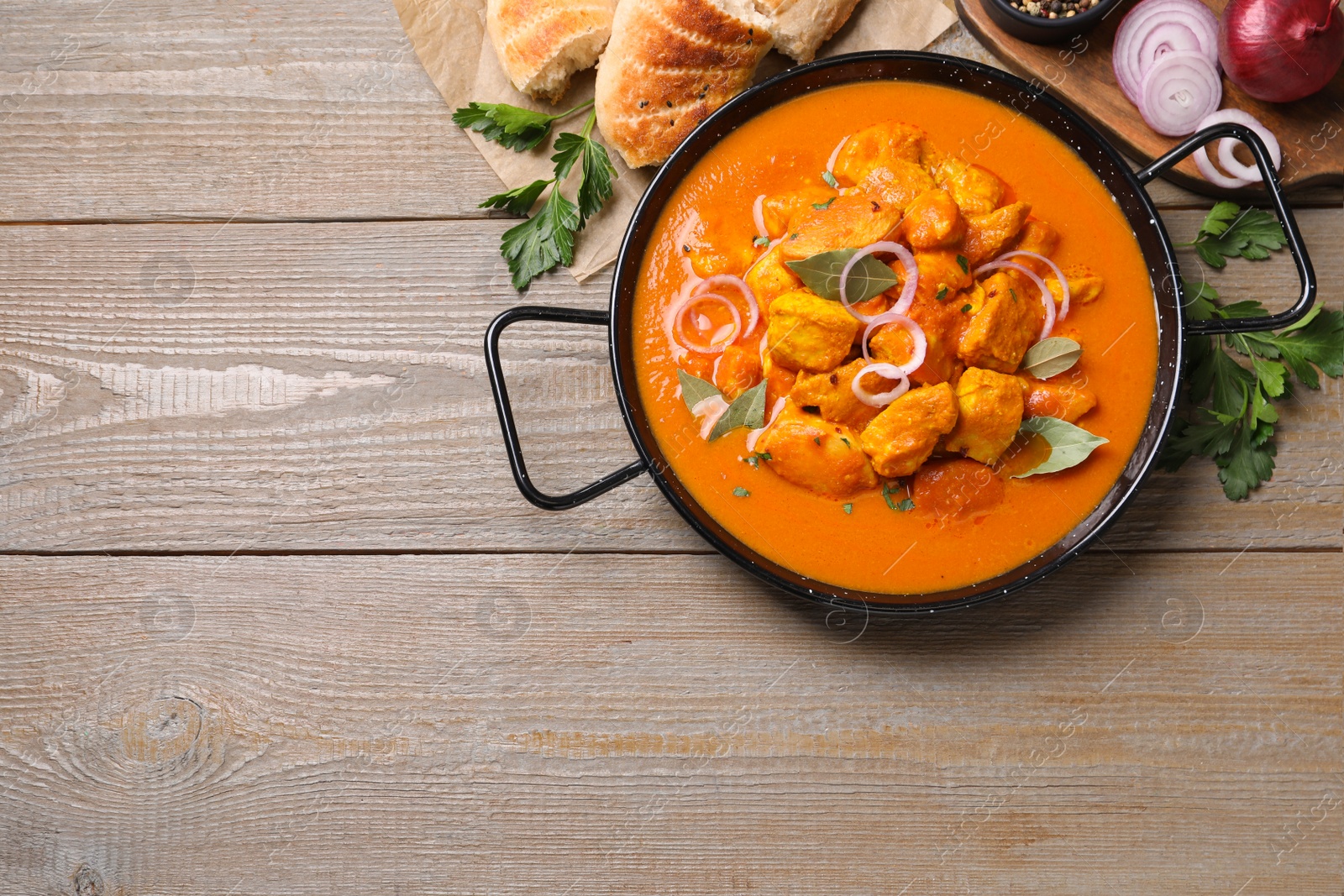 Photo of Delicious chicken curry in pan on wooden table, flat lay. Space for text