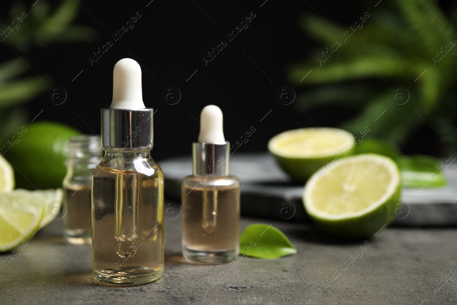 Photo of Lime essential oil and cut citrus fruits on grey table. Space for text