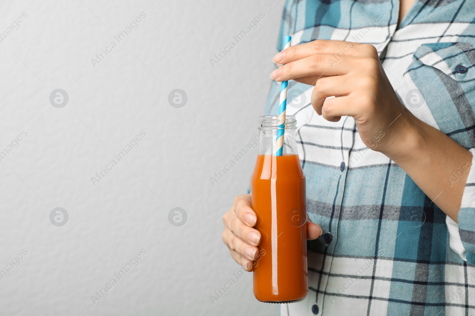 Photo of Woman holding bottle of tasty carrot juice on grey background, closeup. Space for text