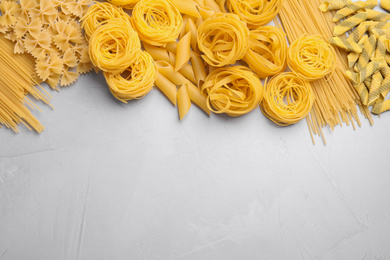 Photo of Different types of pasta on light grey table, flat lay. Space for text